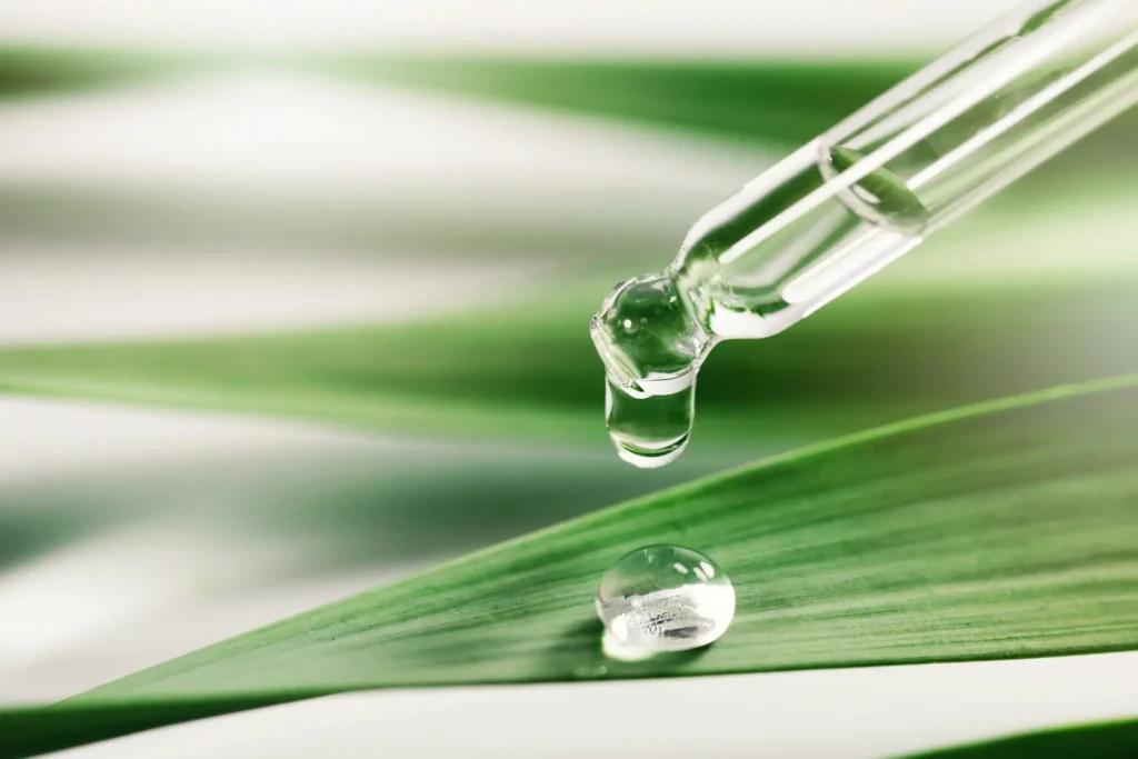 Dropper releasing liquid onto a green leaf, representing skincare ingredients or biotechnology.