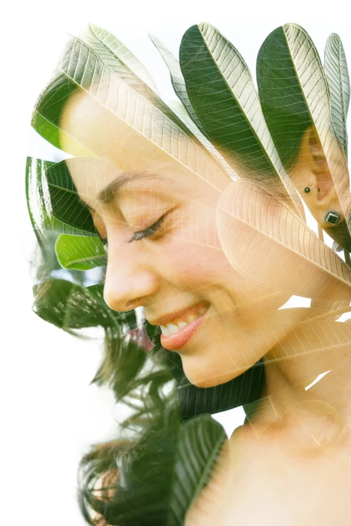 Smiling woman with green leaves, representing natural skincare and wellbeing.