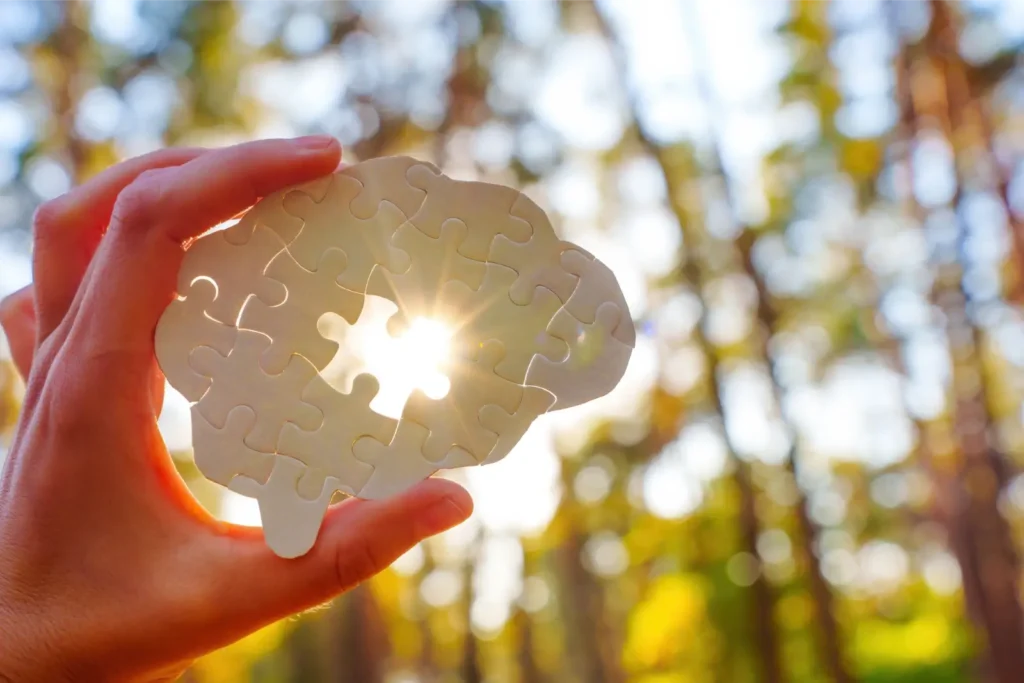 Hand holding glowing puzzle-shaped brain in sunlight