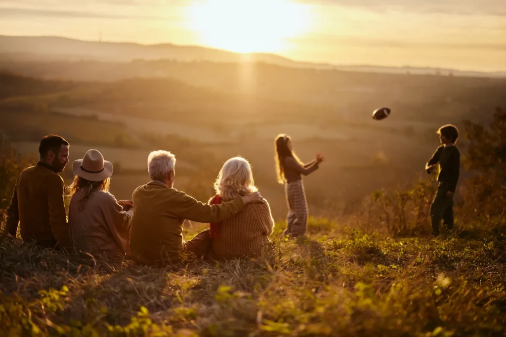 Family sitting together in a grassy field at sunset with warm golden light.